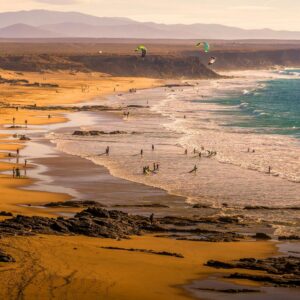Enjoy a lively beach with kitesurfers and scenic cliffs at sunset, perfect for vacation wallpaper.